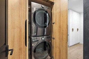 A laundry room with two stacked front-loading washing machines, a wooden door, and a white closet in the background.