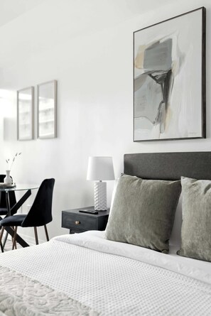 A modern hotel room with a large bed, a desk with a chair, and a nightstand with a lamp. - Modern City Retreat in the Heart of Toronto | Parking Available (Toronto)