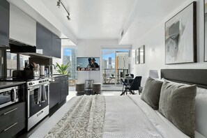 A modern living room with a kitchen, a large flat-screen TV, and a city view. - Modern City Retreat in the Heart of Toronto | Parking Available (Toronto)