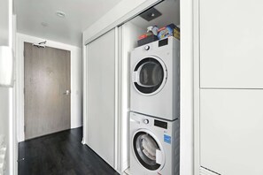 A laundry room with two stacked front-loading washing machines, a wooden door, and a white wall. - Modern City Retreat in the Heart of Toronto | Parking Available (Toronto)