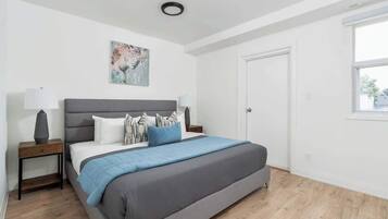 Quarto com cama, mesas de cabeceira, um quadro, uma porta e uma janela.