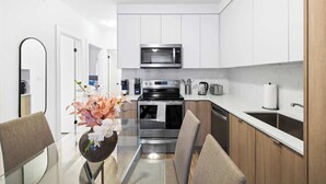 Una cocina moderna con gabinetes blancos, electrodomésticos de acero inoxidable y una mesa de comedor de vidrio con sillas.