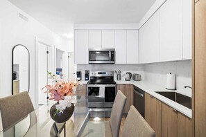 A modern kitchen with white cabinets, stainless steel appliances, and a glass dining table with chairs. - Spacious Bloordale Condo | Quick Transit Access (Toronto)