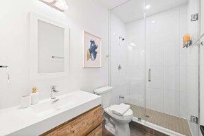 A modern bathroom with a white sink, wooden vanity, a toilet, and a glass shower enclosure. - Spacious Bloordale Condo | Quick Transit Access (Toronto)