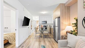 Una cocina moderna con electrodomésticos de acero inoxidable, un comedor con una mesa de vidrio y una sala de estar con un sofá y una planta.
