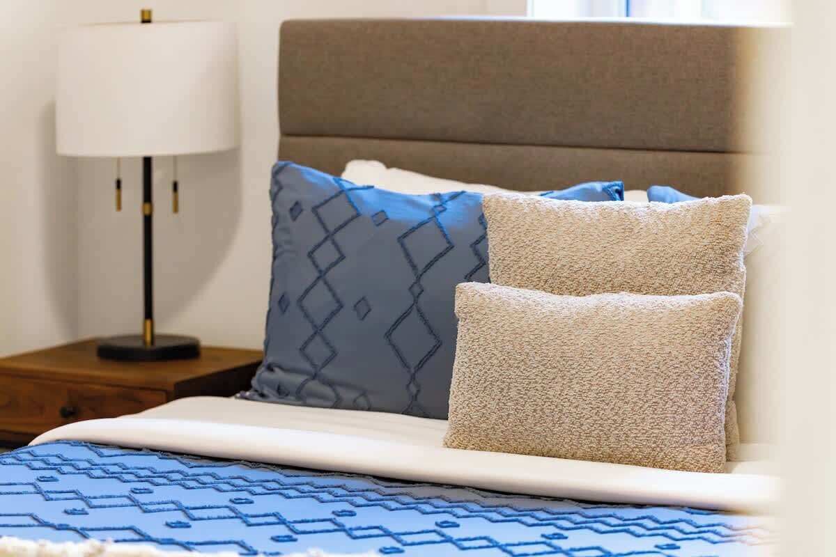 A bed with a patterned bedspread, two pillows, a bedside lamp, and a nightstand.
