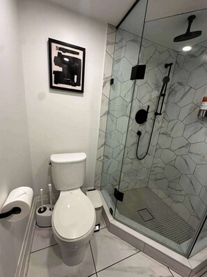 Een moderne badkamer met een douchecabine van glas, een toilet en een lijstwerk kunstwerk aan de wand.