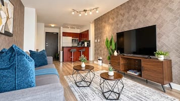 A modern living room with a sofa, coffee table, TV, and a kitchen in the background.