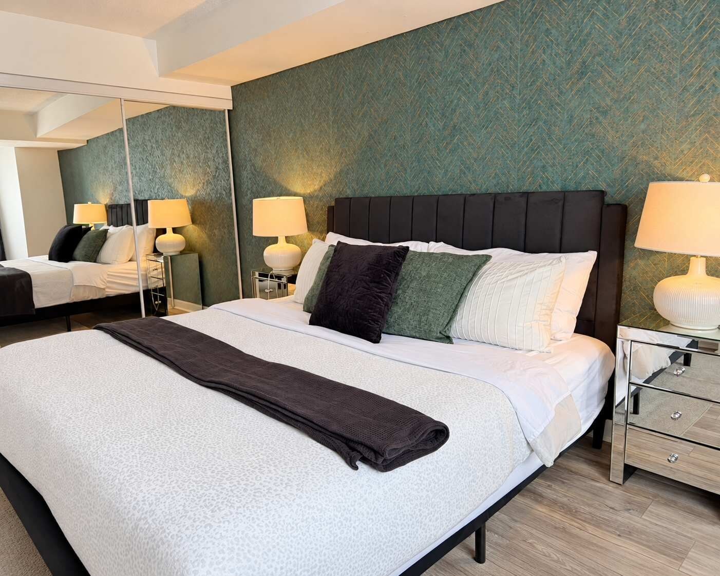 A hotel room with a large bed, two bedside tables with lamps, a mirror, and a green textured wall.