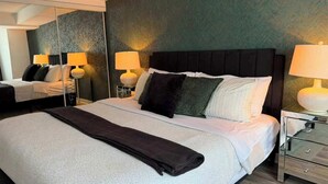 A modern hotel room with a large bed, bedside lamps, a mirror, and a wooden floor.