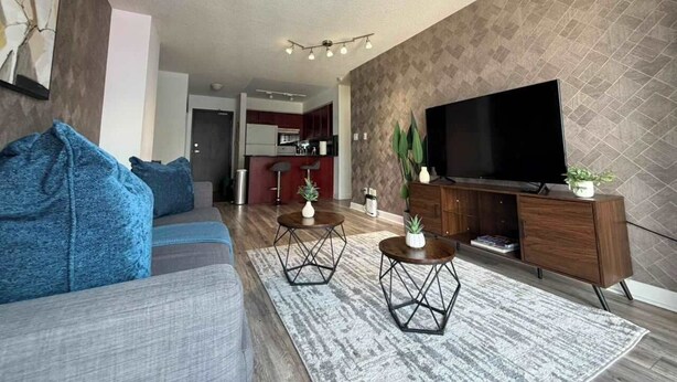 A modern living room with a sofa, coffee table, TV, and a kitchen in the background.