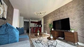 A modern living room with a sofa, coffee table, TV, and a kitchen in the background.