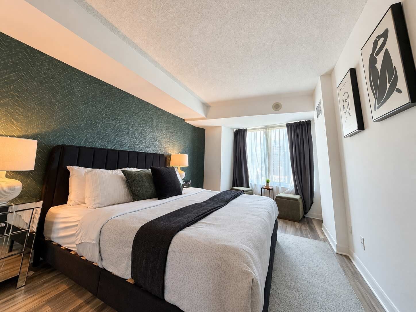 A hotel room with a bed, bedside tables, a window with curtains, and artwork on the wall.