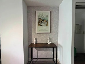 A framed artwork of Paul Cezanne's 'The Basket of Apples' on a wall above a dark wooden table with two white vases.
