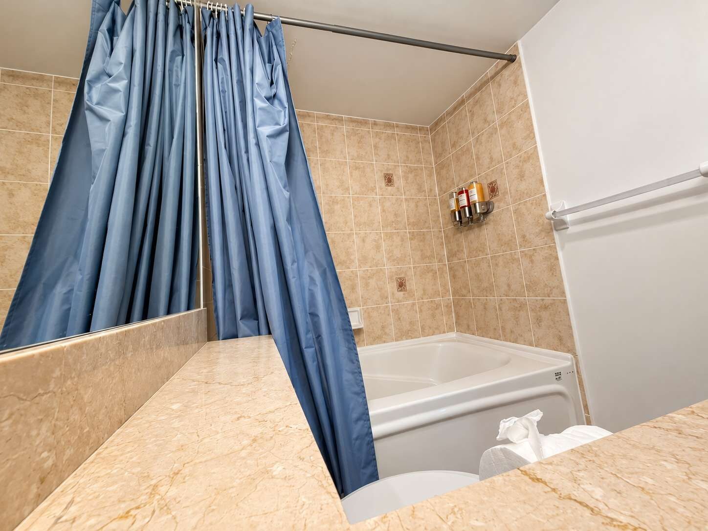 A bathroom with a bathtub, a marble countertop, and a blue shower curtain.