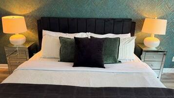 A bed with a black headboard, white and green pillows, and a black throw blanket. There are two bedside tables with lamps.
