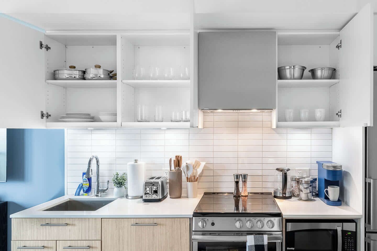 A modern kitchen with white cabinetry, a stainless steel range, a built-in oven, a microwave, and a coffee machine.