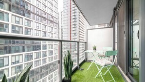 Un balcón con piso de césped artificial, una pequeña mesa con una silla y plantas en macetas.