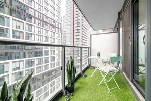 Ein Balkon mit grünem Kunstrasenteppich, einem Tisch, einem Stuhl und Topfpflanzen.