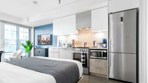 Un dormitorio moderno con una cama grande, una cocina con electrodomésticos de acero inoxidable y vistas a la ciudad.