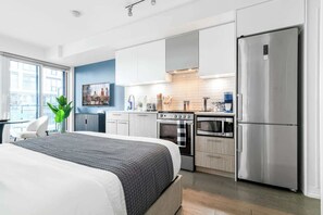 Une chambre moderne avec un grand lit, une cuisine équipée d’appareils électroménagers en acier inoxydable et une vue sur la ville.