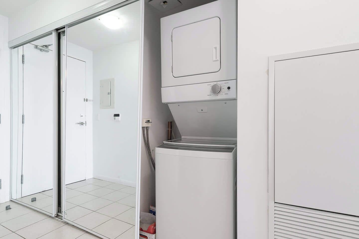 Une buanderie équipée d’un lave-linge et d’un sèche-linge à chargement frontal, d’une porte-fenêtre coulissante et d’un sol carrelé.
