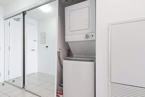 A laundry room with a front-loading washer and dryer, a sliding glass door, and a tiled floor.