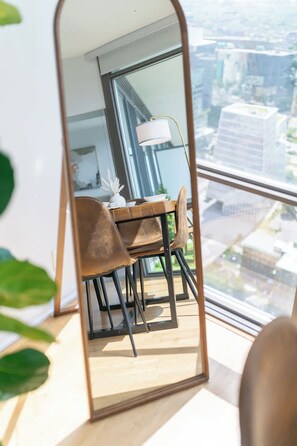 Ein Essbereich mit Tisch und Stühlen, einer Lampe und Blick auf die Stadt durch große Fenster.