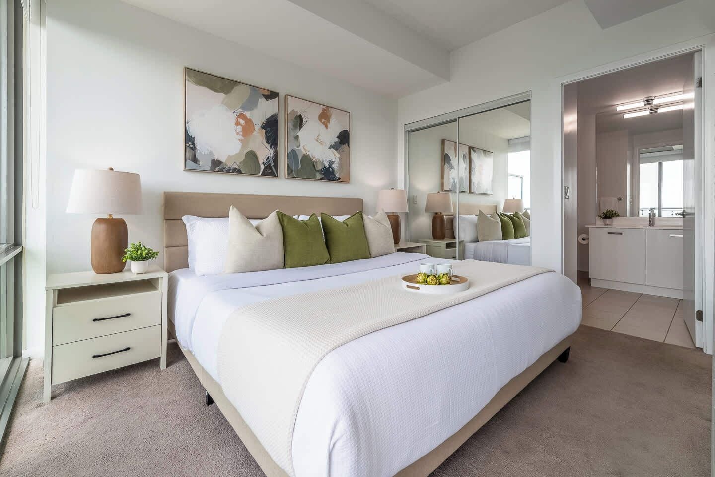 A modern bedroom with a large bed, bedside tables, a mirror, and artwork on the wall.