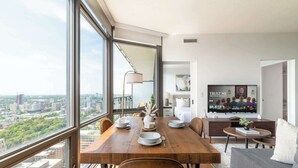 A modern dining area with a city view, a television displaying a program, and a cozy seating area with a sofa. - Financial District 3BR CN Tower Views! (Toronto)