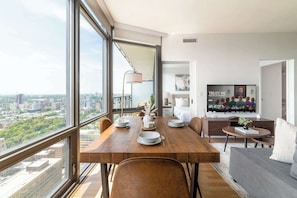 Ein moderner Essbereich mit Stadtblick, einem Fernseher, der ein Programm zeigt, und einer gemütlichen Sitzecke mit einer Couch.