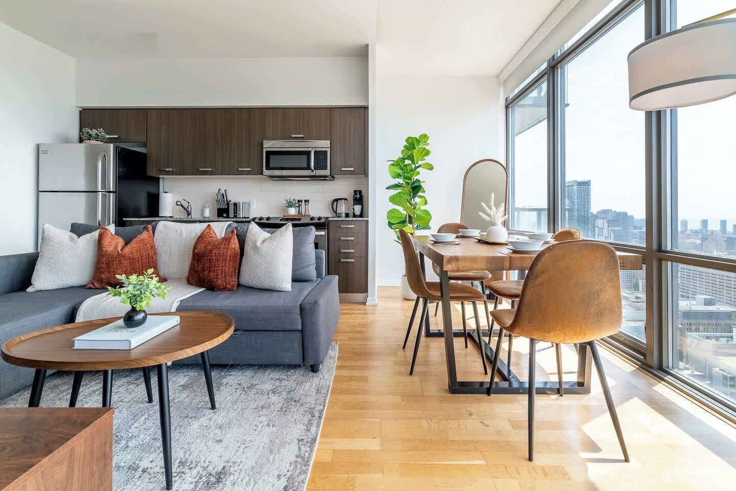 Un appartement moderne comprenant un espace de vie, une cuisine, un coin repas et de grandes fenêtres offrant une vue sur la ville.