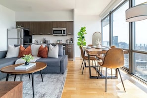 A modern apartment with a living area, kitchen, dining space, and large windows offering a city view.