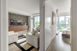 A modern living room with a sofa, coffee table, and a TV mounted on a textured wall. - Upscale 3BR Downtown Suite with Parking! | Parking Available (Toronto)