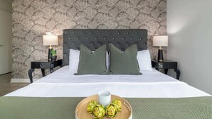 A hotel room with a tufted headboard, two bedside tables with lamps, a bed with white linens, and a tray with fruits on the bed. - Upscale 3BR Downtown Suite with Parking! (Toronto)