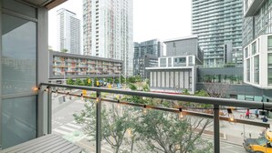 A balcony with a view of a cityscape, including modern buildings and a street with vehicles. - Upscale 3BR Downtown Suite with Parking! (Toronto)