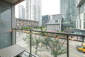 Ein Balkon mit Blick auf eine Stadtlandschaft, darunter moderne Gebäude und eine Straße mit Fahrzeugen.
