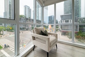 A modern room with a large window, a beige armchair, and a view of a cityscape. - Upscale 3BR Downtown Suite with Parking! | Parking Available (Toronto)