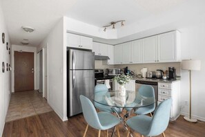 A modern kitchen with white cabinets, stainless steel appliances, and a glass dining table with blue chairs.