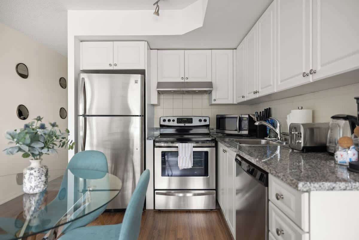 A modern kitchen with stainless steel appliances, white cabinetry, and a glass dining table.