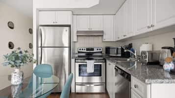 A modern kitchen with stainless steel appliances, white cabinetry, and a glass dining table.