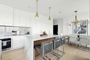 A modern kitchen with white cabinetry, a marble island, bar stools, and pendant lighting. - 2BR Entertainment District Hub | Balcony & Parking | Parking Available (Toronto)