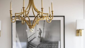 Uma sala de jantar com lustre, duas cadeiras, uma mesa e uma fotografia em preto e branco emoldurada na parede.