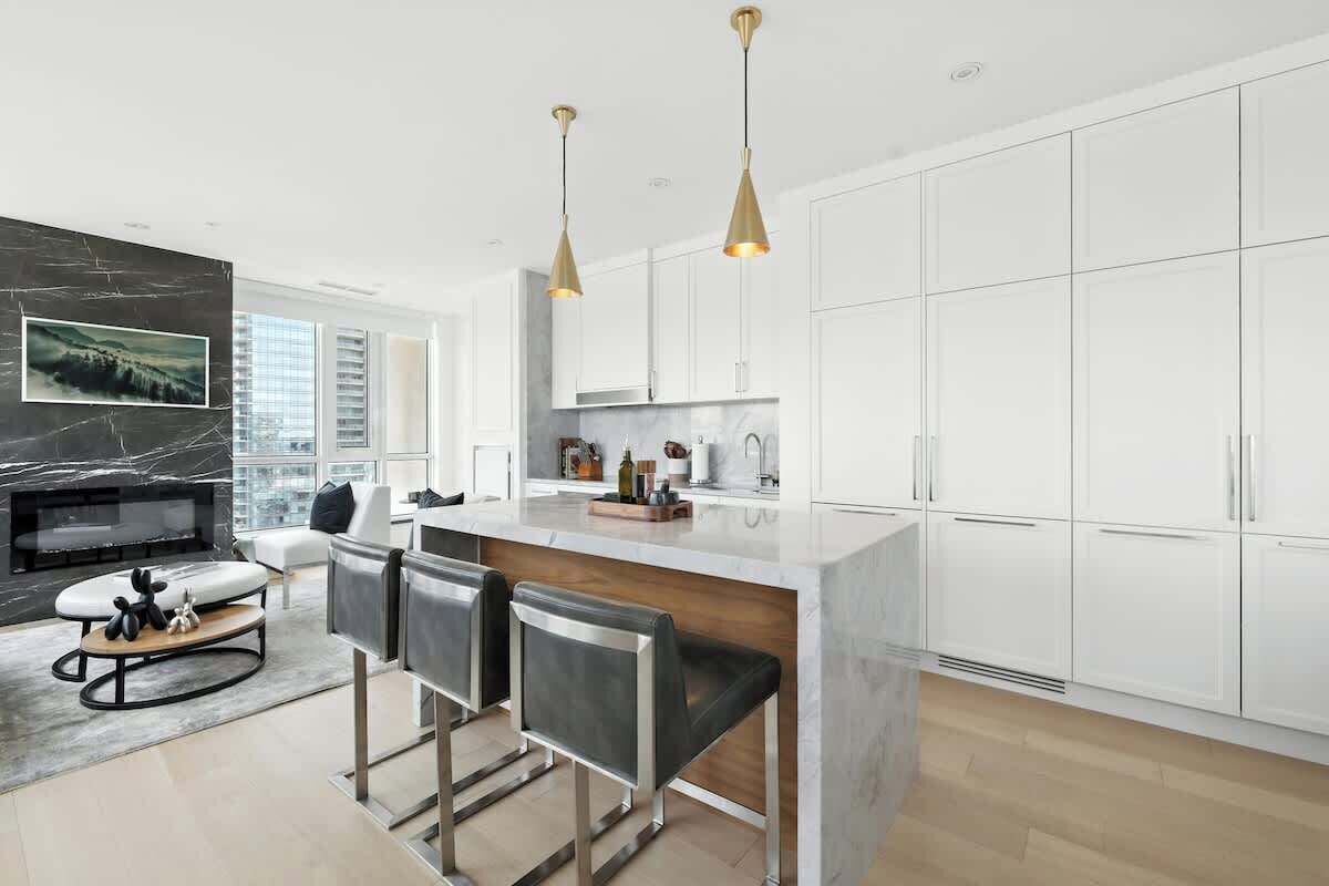 A modern kitchen with white cabinets, a marble island, and pendant lighting.