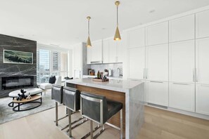 A modern kitchen with white cabinets, a marble island, and pendant lighting. - 2BR Entertainment District Hub | Balcony & Parking | Parking Available (Toronto)