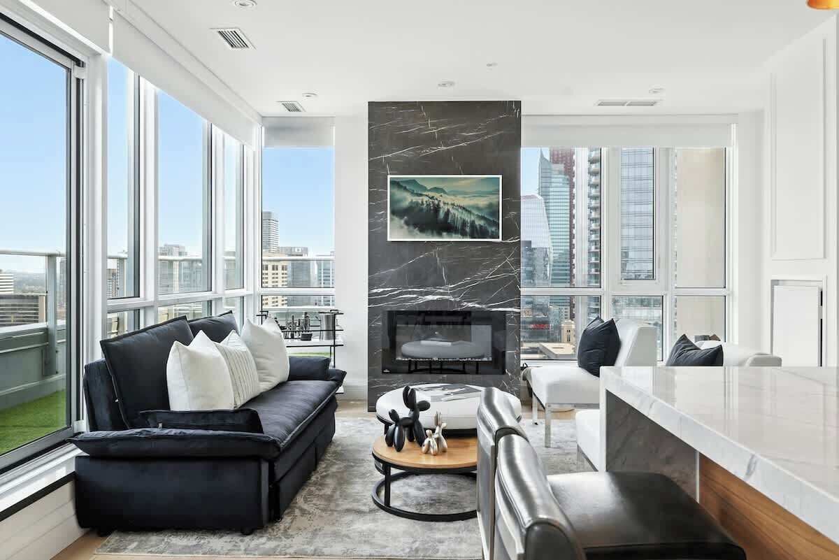 A modern living room with a fireplace, a sofa set, and a dining area with a view of the city.