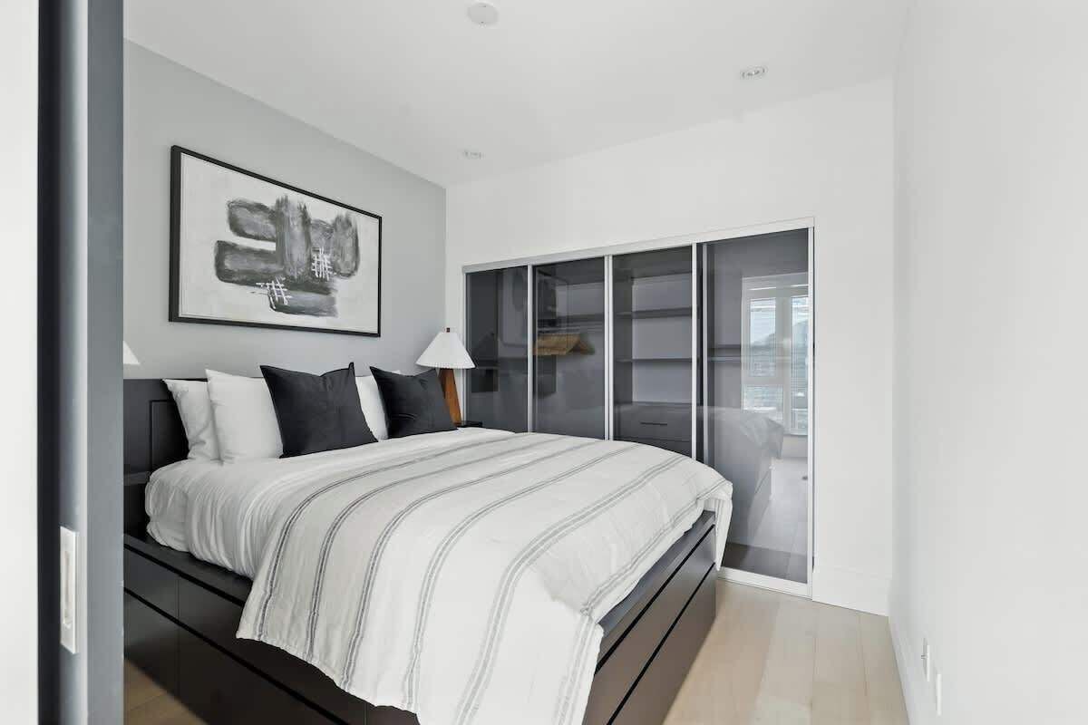 A modern bedroom with a bed, a large window, and a framed artwork on the wall.