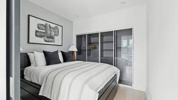 A modern bedroom with a bed, a large window, and a framed artwork on the wall.