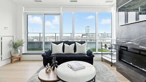 Uma sala de estar moderna com um sofá preto, uma mesa de centro redonda e uma grande janela com vista para a cidade.