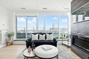 Ein modernes Wohnzimmer mit einem schwarzen Sofa, einem runden Couchtisch und einem großen Fenster mit Blick auf die Stadt.